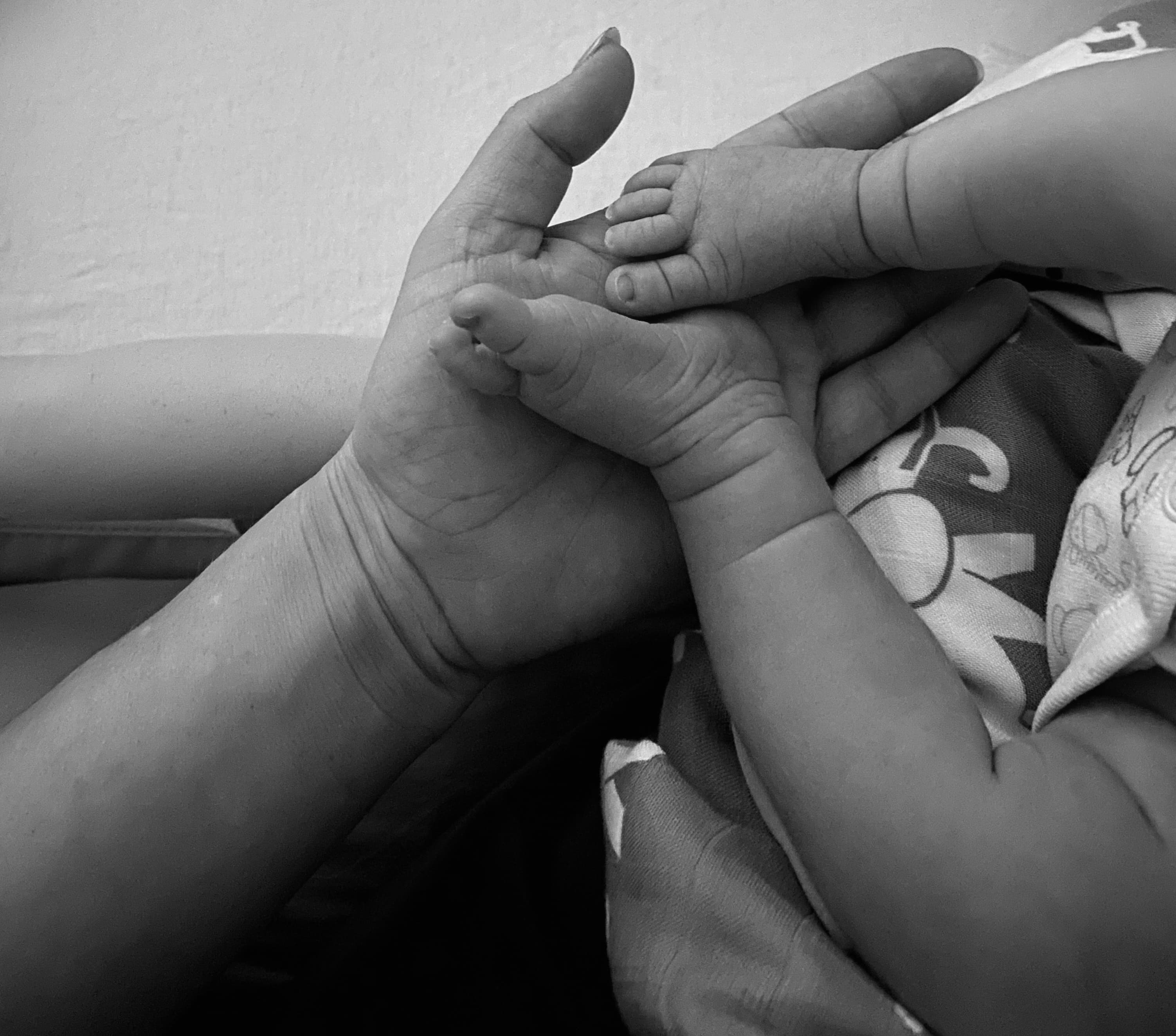 An adult hand cradling a baby's hand and foot