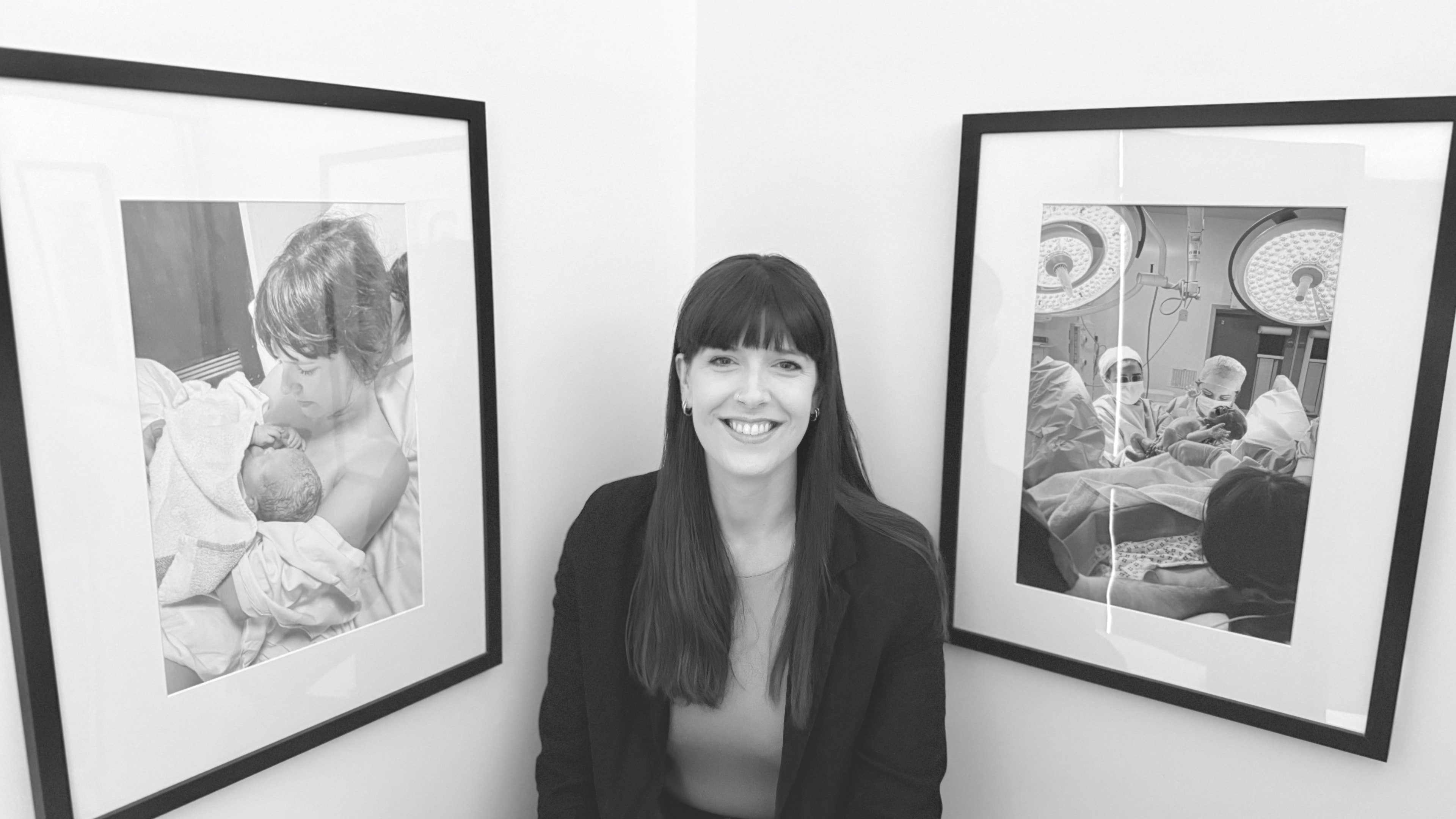 Hannah, founder of Tell Me Again, seated between two framed photographs from her own children's births